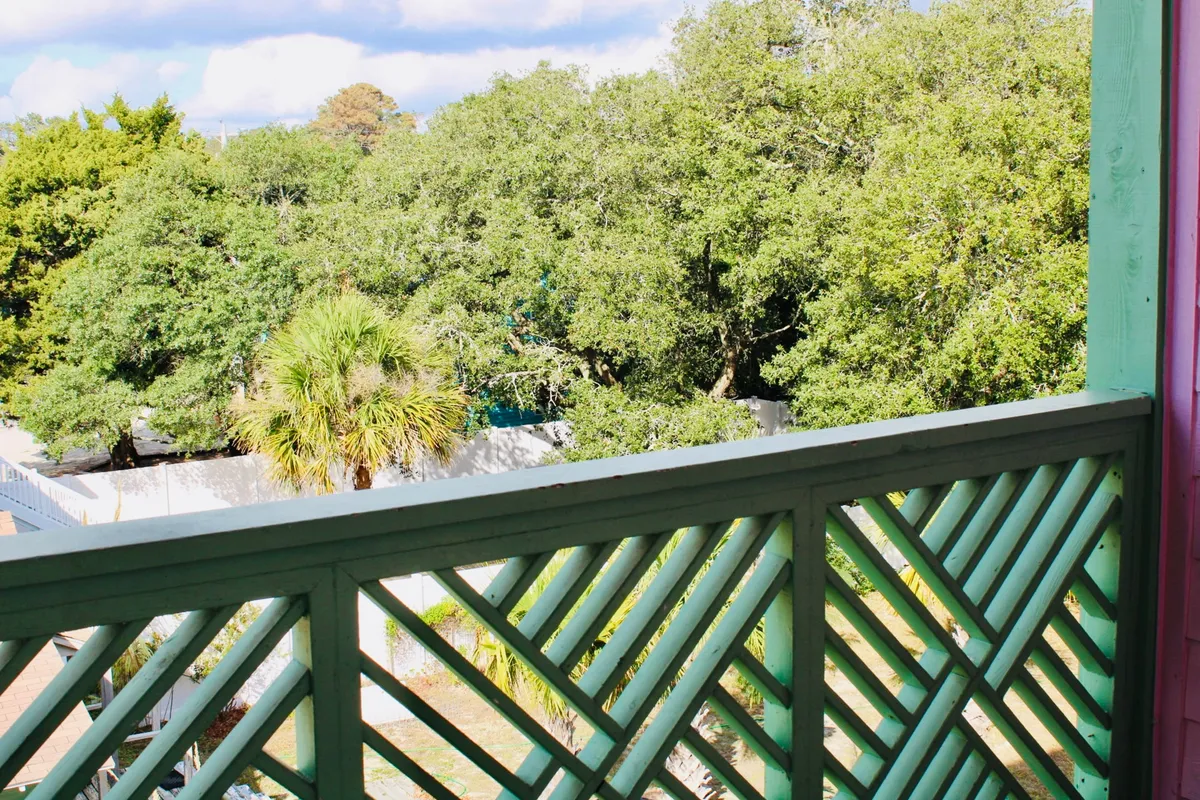 A serene view framed by lush palm trees and greenery, with an architectural railing in the foreground. The tranquil scene suggests relaxation and a strong connection to the coastal environment, offering glimpses of sunrise and nature just outside.
